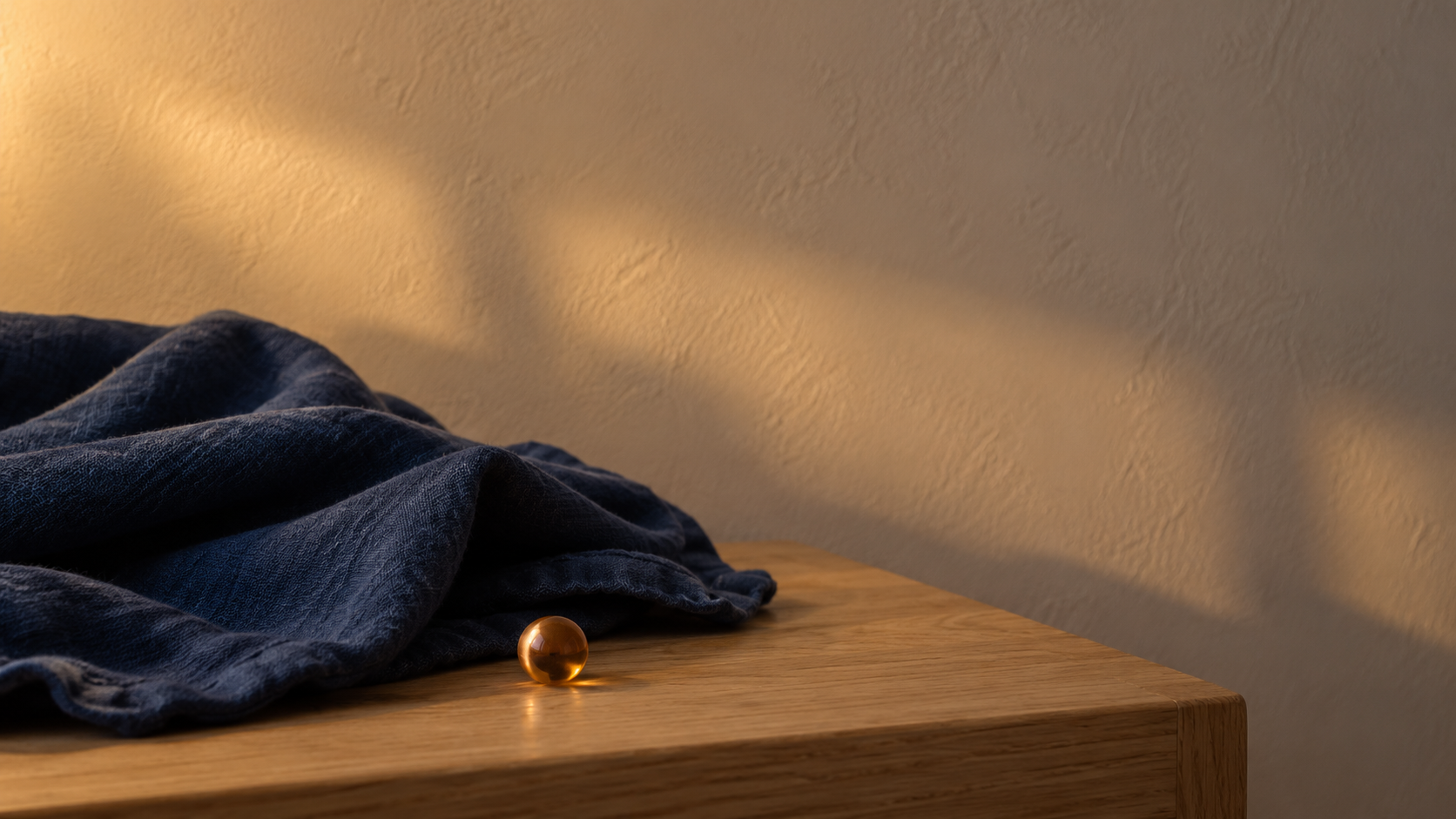 A folded indigo linen cloth resting on a warm cream bedside surface in gentle low evening light.